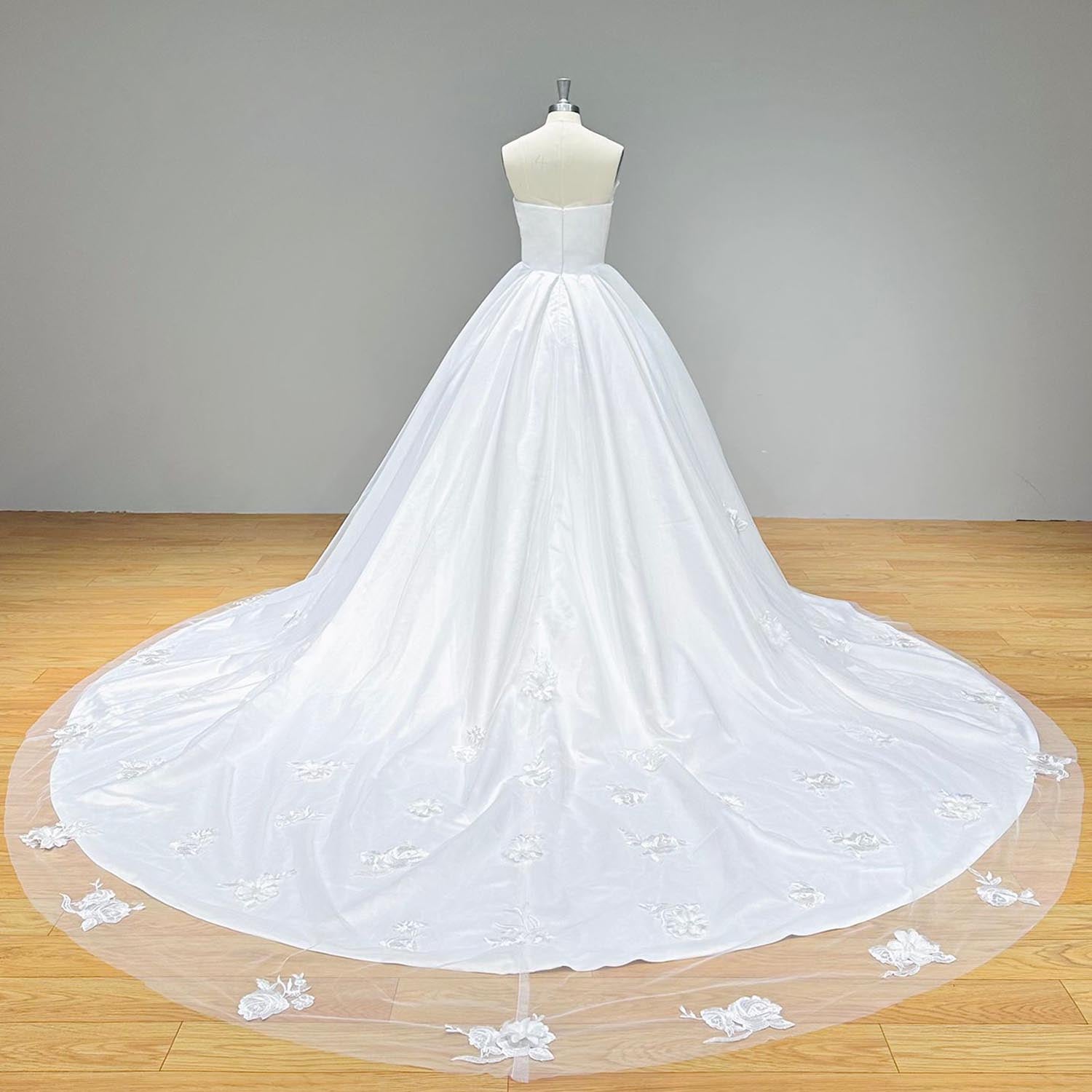 Dramatic full back view of a luxury satin ball gown wedding dress on a mannequin, perfectly displaying the clean zipper back closure and a wide sweeping train adorned with delicate floral lace appliques.