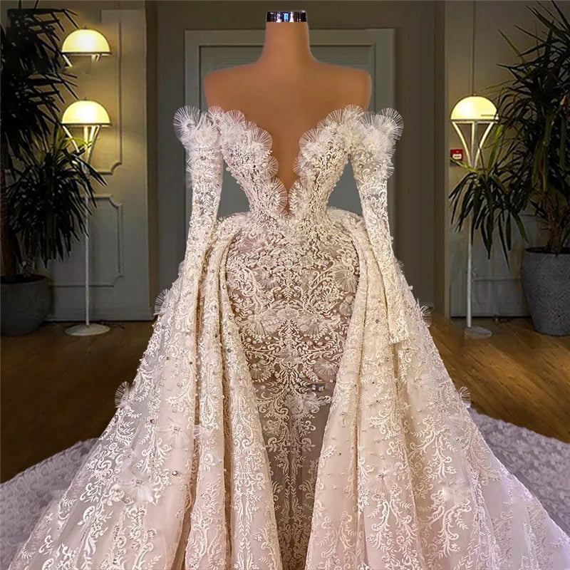 Detailed studio shot of an off-the-shoulder Arabic bridal gown bodice on a dress form, highlighting the intricate mesh frill trim along the neckline, long lace sleeves, and structured corset waist.