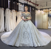 Beautiful bride holding a white rose, wearing a luxury off-the-shoulder beaded wedding gown with an elegant ball gown silhouette and dramatic long train.