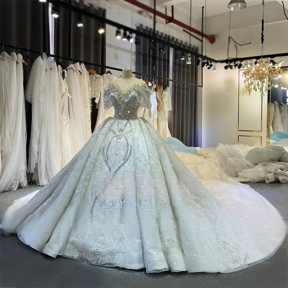 Full angled view of the luxury off-the-shoulder beaded wedding dress on a mannequin in a bridal shop, emphasizing the grand scale of the sparkling train.