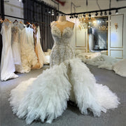 Front view of a luxury mermaid wedding dress on a mannequin, featuring heavy pearl and crystal beading, a deep V-neckline, and a dramatic ruffled tulle skirt with a high leg slit.