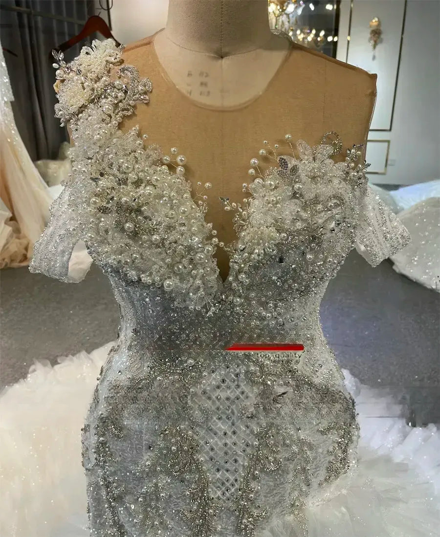 Close-up detail of a bridal gown bodice showcasing intricate hand-beaded pearls, crystal embellishments, floral lace appliques, and a delicate illusion mesh neckline.
