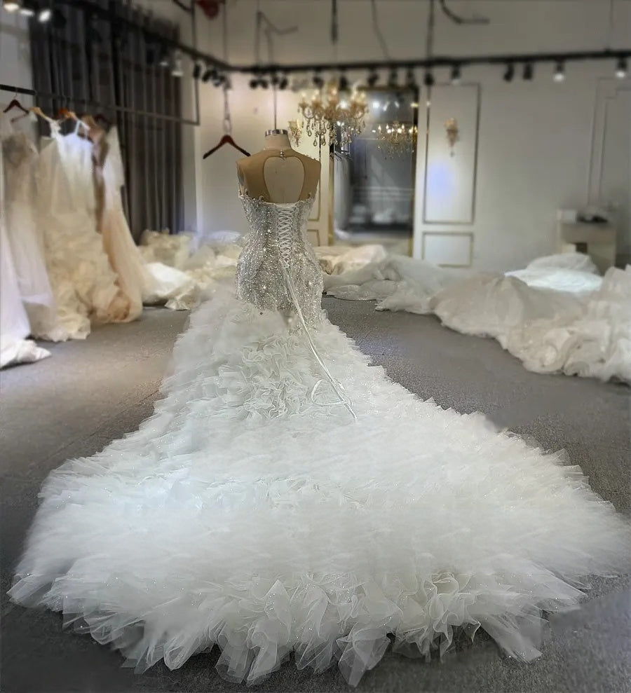 Detailed rear view of a custom mermaid wedding dress on a mannequin, emphasizing the intricate beadwork, adjustable lace-up back, and the massive scale of the ruffled train.