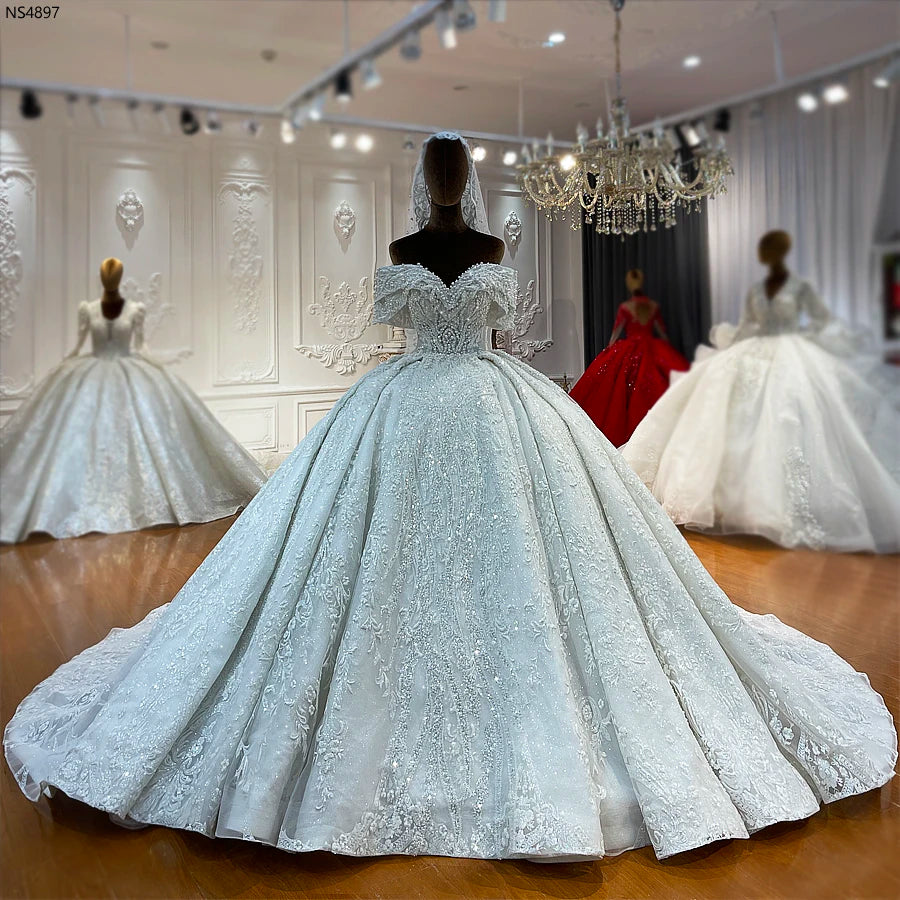 Front-facing view of a designer off-the-shoulder wedding gown on a mannequin, showcasing detailed pearl and lace embroidery.