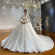 Full-length front view of an elegant model in a luxury off white lace Muslim ball gown wedding dress featuring intricate floral embroidery, long sleeves, and a majestic cathedral train under a crystal chandelier.