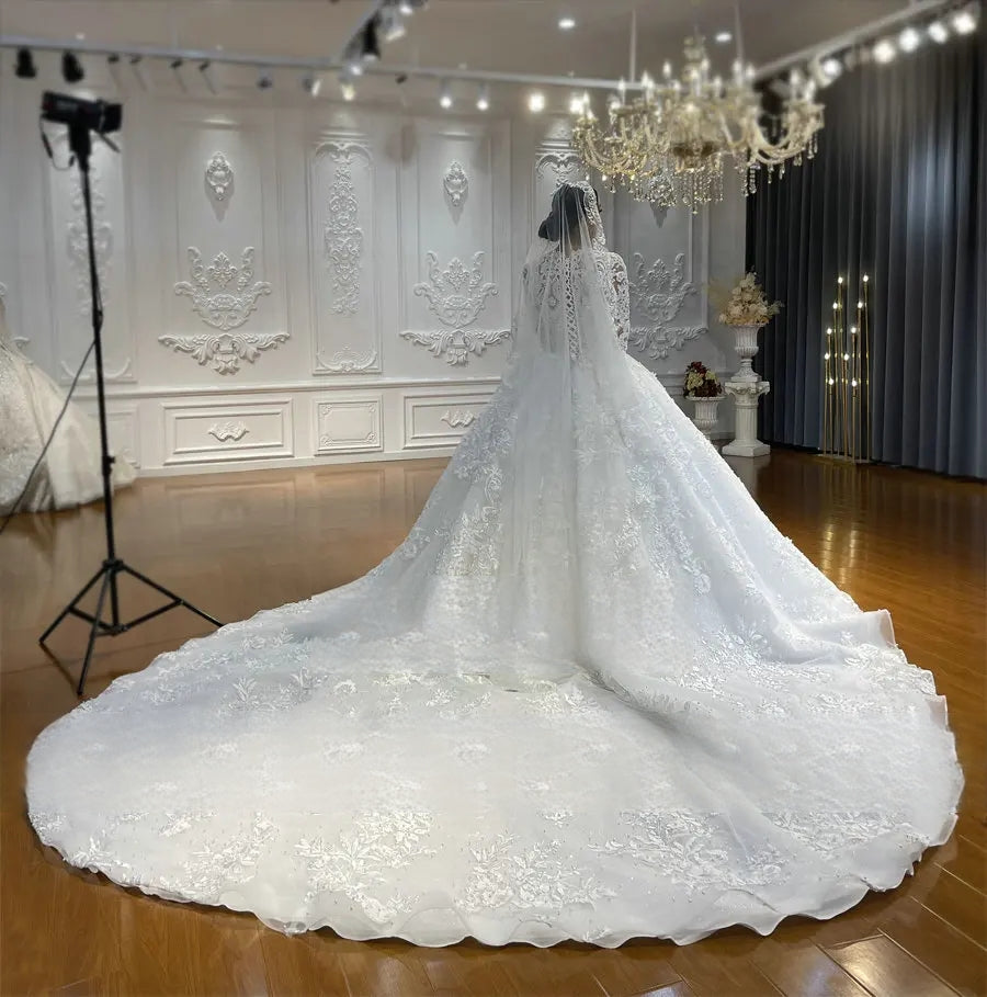 Full rear perspective of a long sleeve lace Muslim bridal gown highlighting the expansive, circular cathedral-length train and a matching sheer lace-edged veil in a grand showroom.