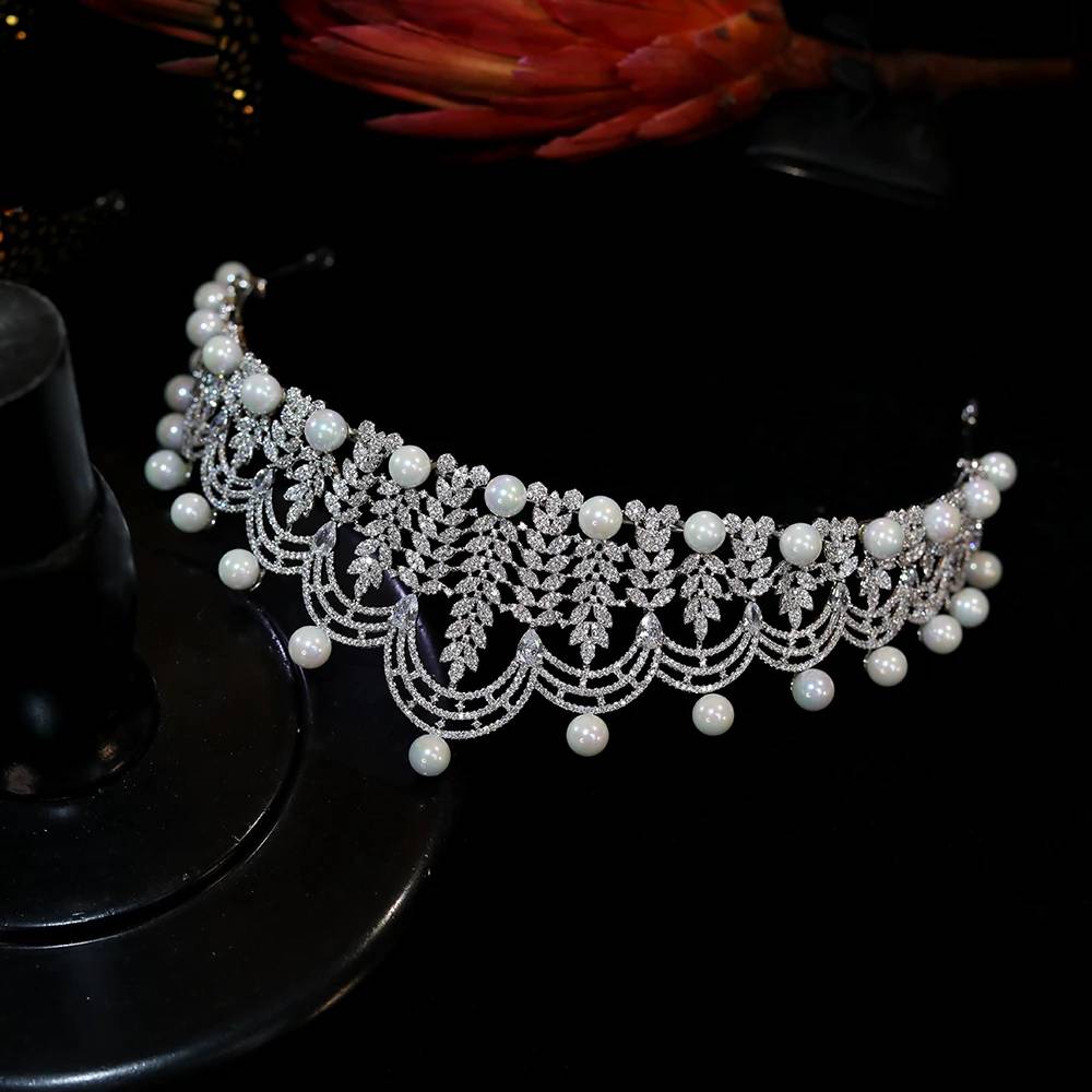Top-down flat lay view of a shimmering pearl crown tiara on a black surface, showcasing its flexible hairband design.