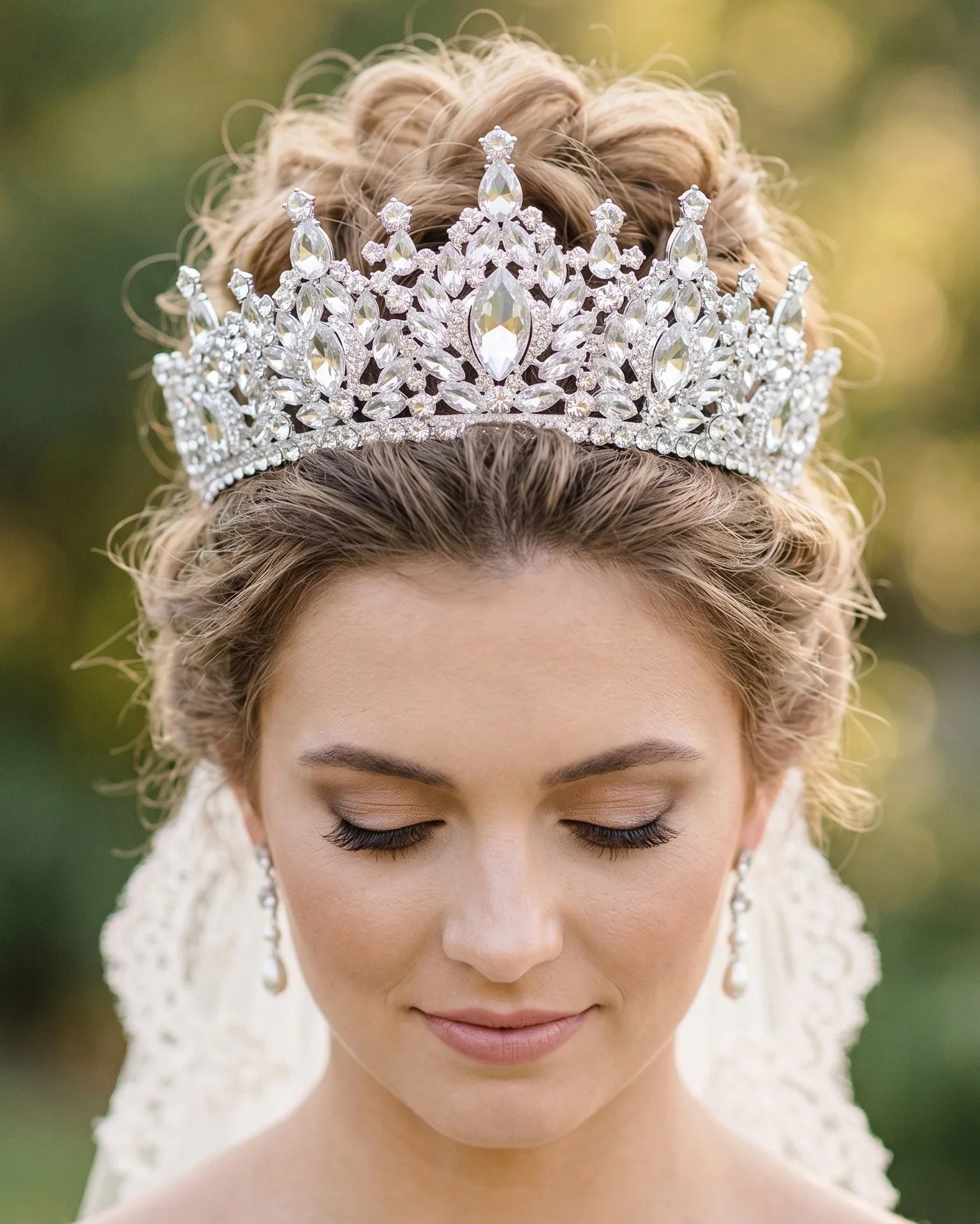 A bride with an elegant updo looking down while wearing a luxury rhinestone bridal tiara crown and crystal headband.