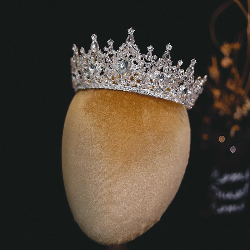 Full view of a majestic silver crystal tiara crown for weddings and prom, showcased on a gold display headrest.