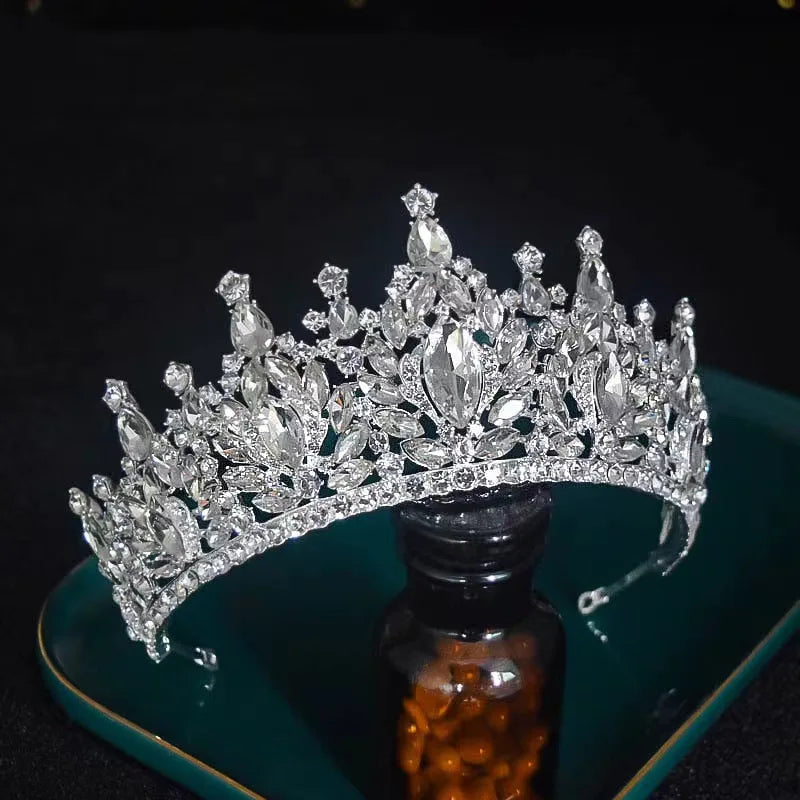 A brilliant crystal headband crown for special occasions resting horizontally across a green display tray next to a dark glass bottle.