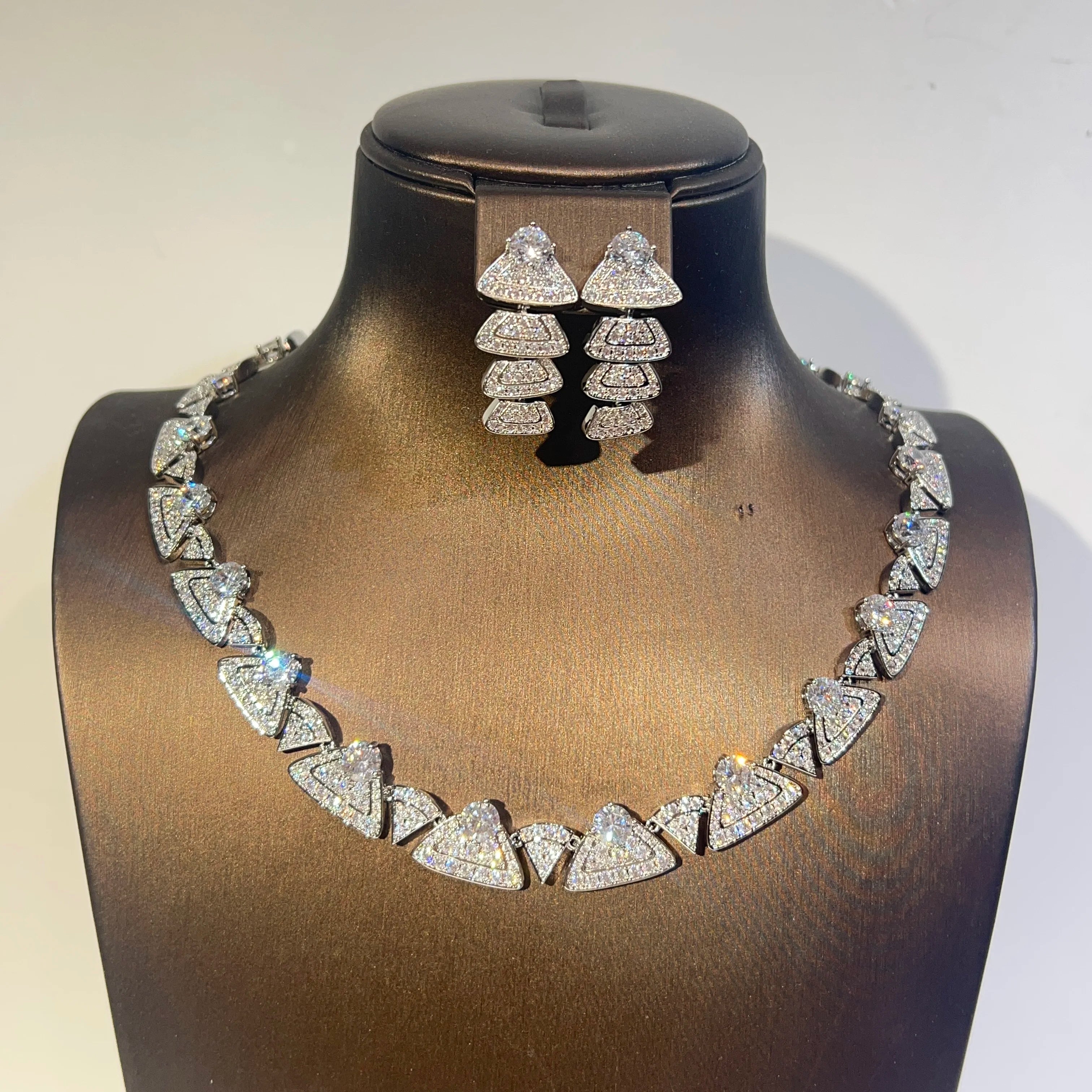 Direct front view of a sparkling cubic zirconia wedding choker necklace and geometric drop earring set on a dark jewelry bust.