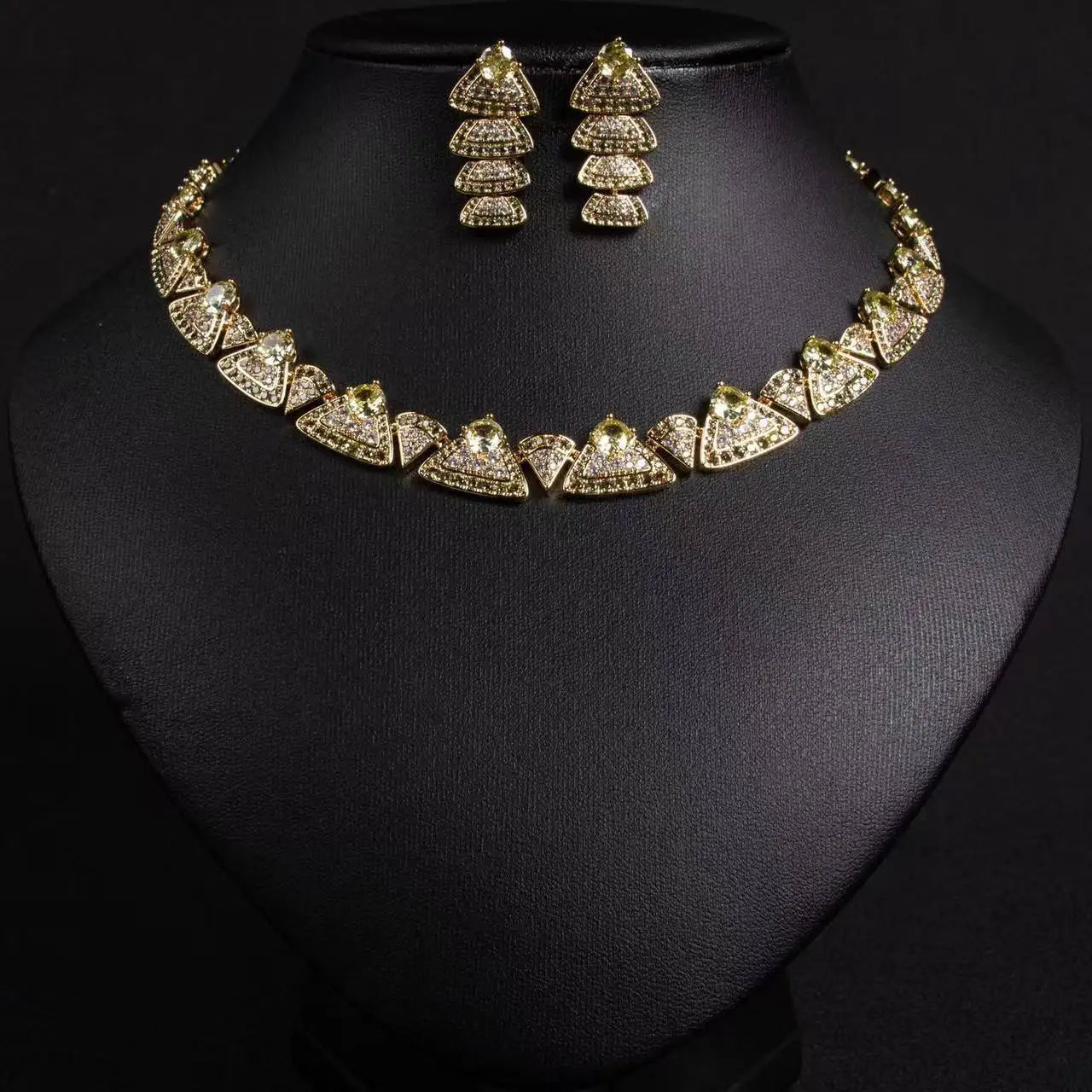 Front profile view of a luxury gold-toned bridal choker necklace and matching tiered earrings set on a black display stand.