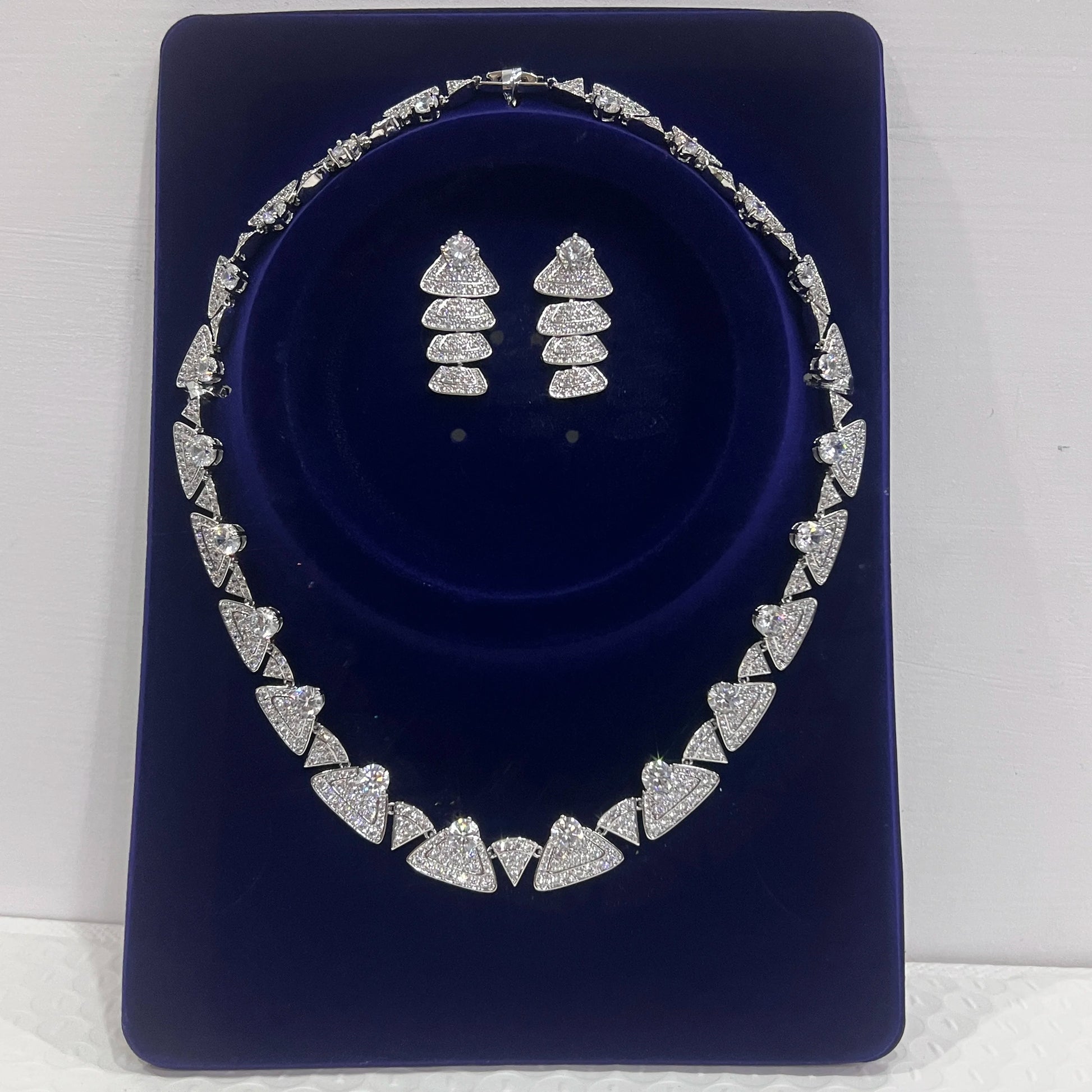 Premium white cubic zirconia bridal choker necklace and matching geometric dropdown earrings presented inside a luxury blue velvet display case.