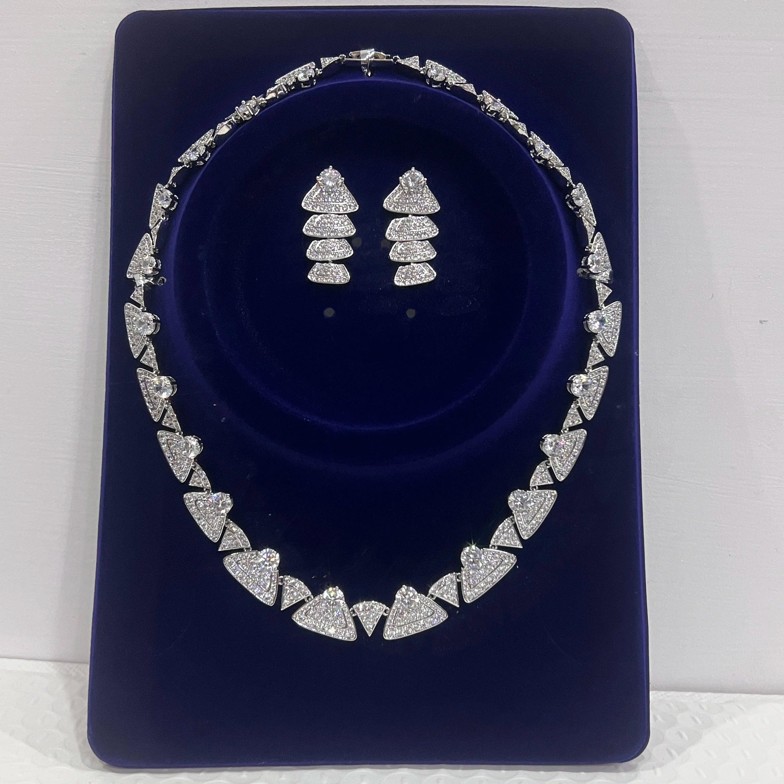 Premium white cubic zirconia bridal choker necklace and matching geometric dropdown earrings presented inside a luxury blue velvet display case.