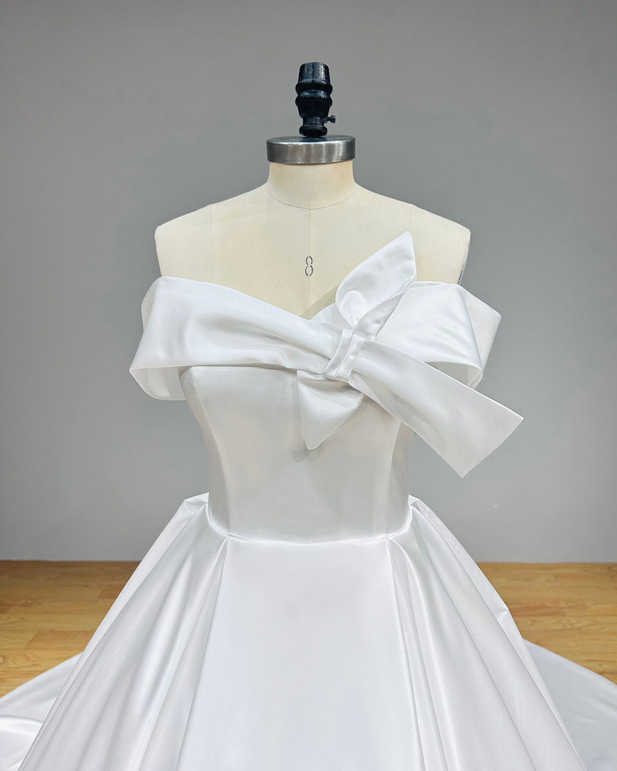 Close-up detail of a structured satin wedding dress bodice highlighting the asymmetric oversized bow detail and flawless tailoring on a couture mannequin.