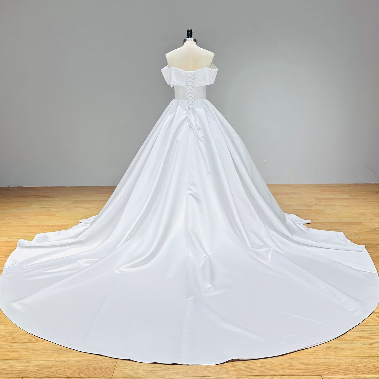 Back view of a minimalist white satin wedding dress on a dress form showcasing a traditional lace-up corset back closure and a sweeping chapel-length train.