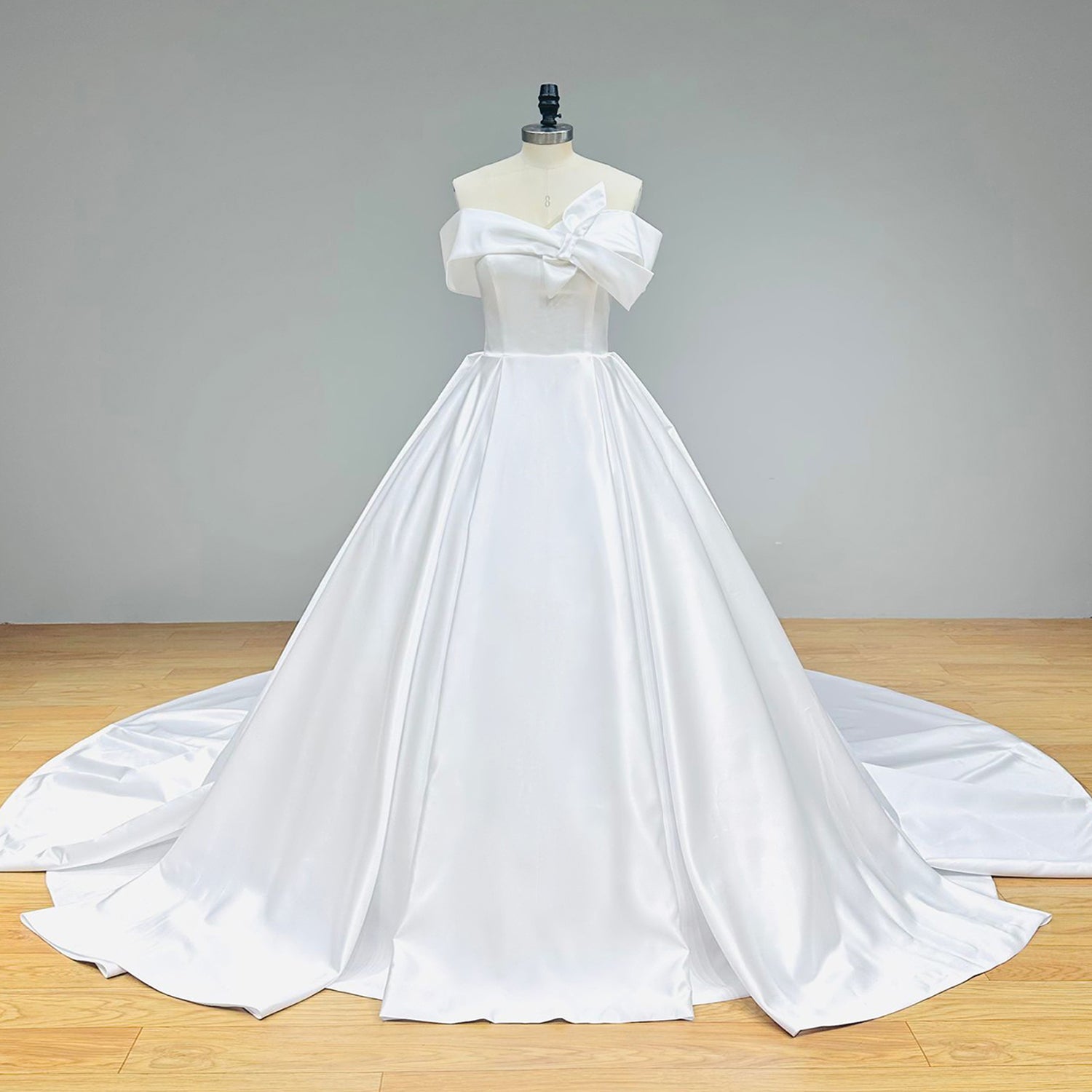 Full-length front view of a heavy satin bridal ball gown featuring box pleating on the voluminous skirt and a structured off-shoulder bodice on a mannequin.