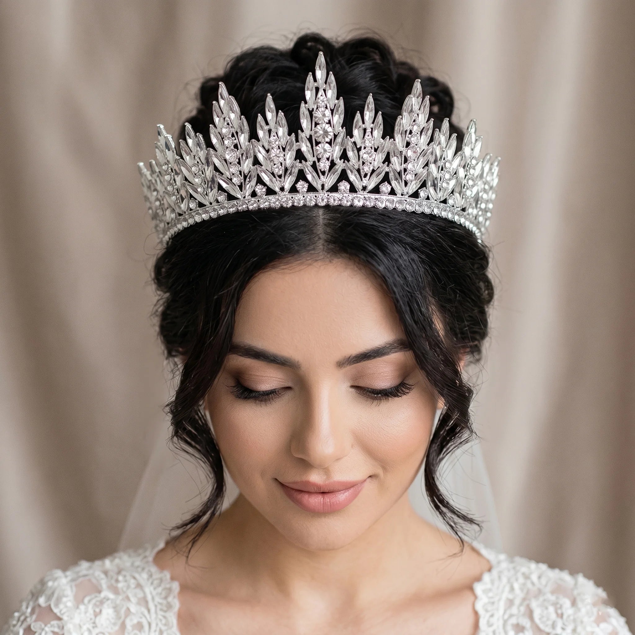 A close-up of a bride with a braided updo looking down, wearing a high-set luxury silver crystal bridal tiara crown.