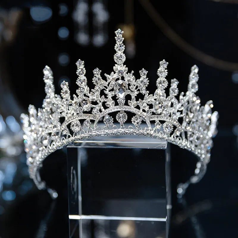 A high-set princess crown wedding headband with geometric crystal patterns and a tall central peak, displayed on a glass block.