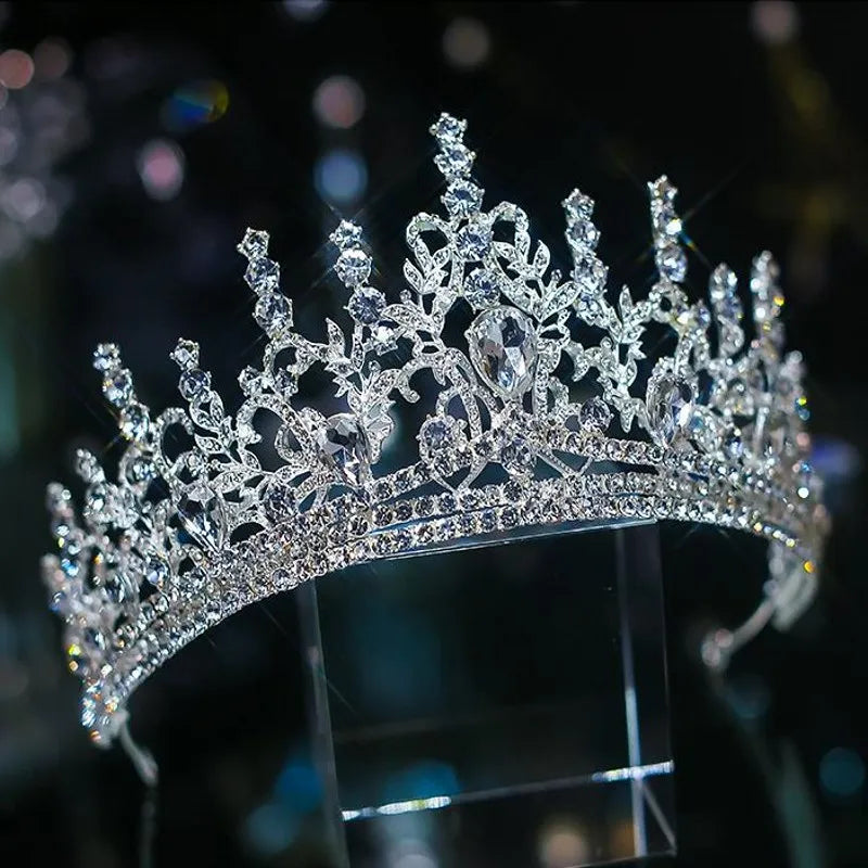 Side angle view of a glittering silver pageant crown heavily adorned with brilliant clear rhinestones and an ornate peak structure.