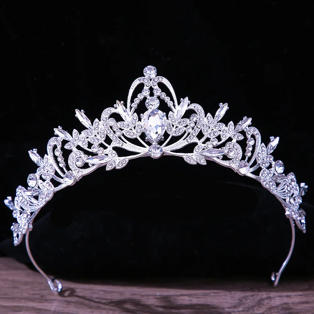 A classic princess pageant tiara with an elevated center arch highlighting a teardrop rhinestone and scrollwork crystal details.