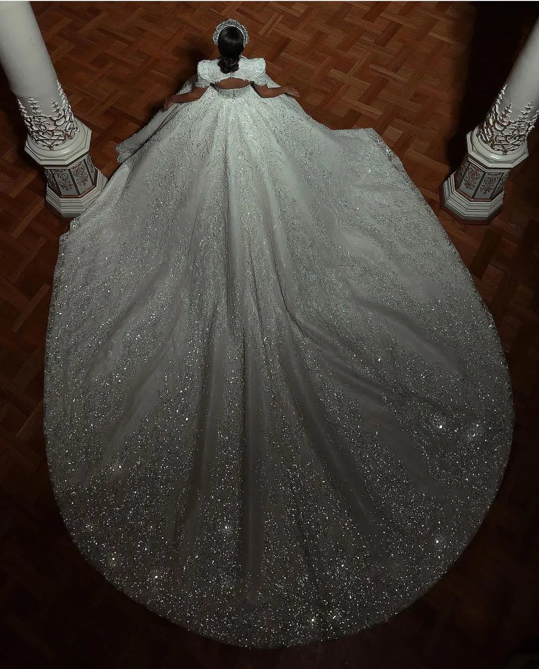 High-angle rear view of a sparkling sequin bridal ball gown showcasing a dramatic sweeping court train heavily scattered with reflective micro-glitter.
