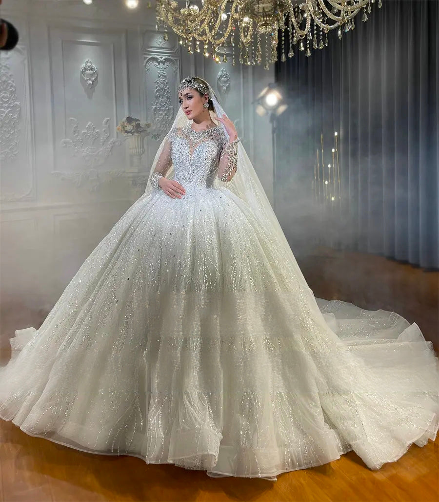 Full-length view of a luxury sparkling bridal gown with a heavily embellished bodice and long sleeves, emphasizing the grand silhouette and reflective beadwork.