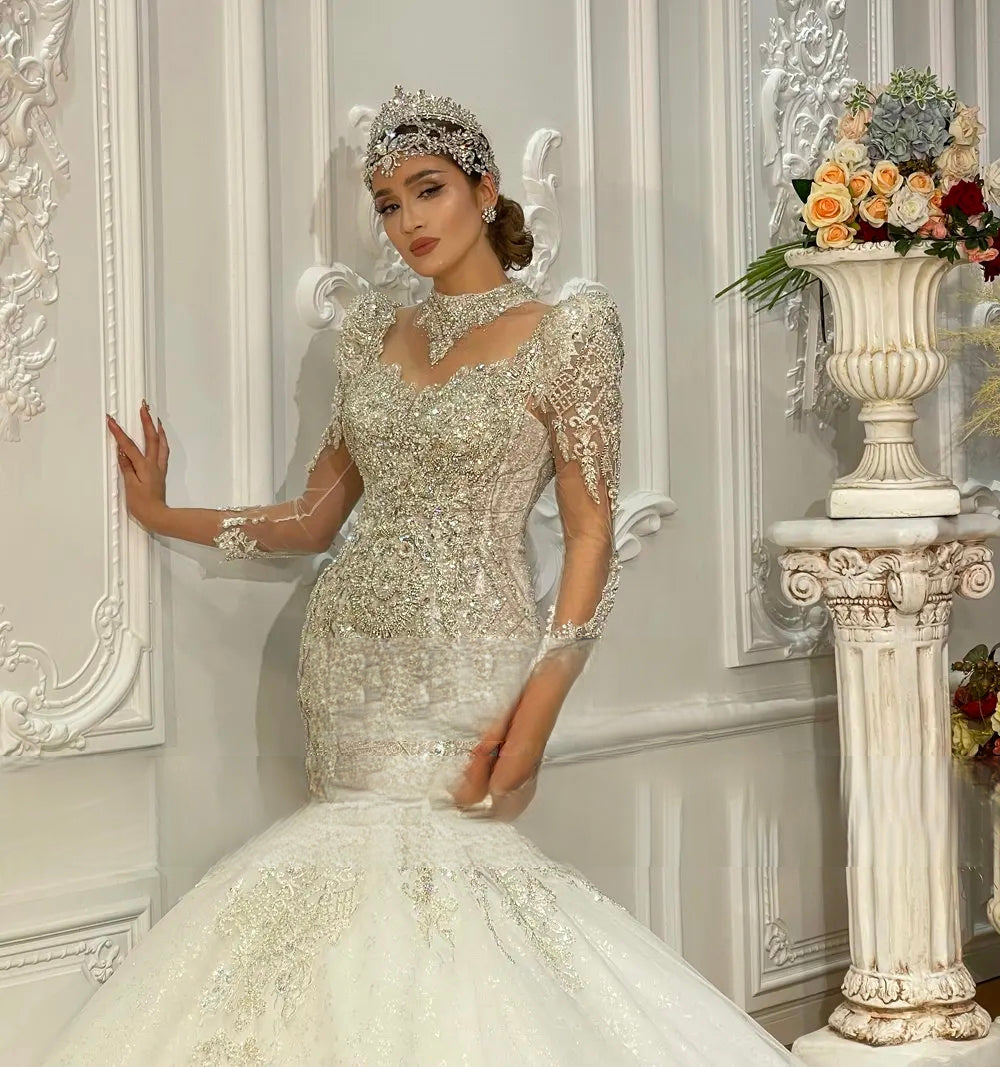 Detailed shot of the 3D crystal-embellished bodice and sheer transparent lace sleeves of a luxury fitted mermaid wedding dress.