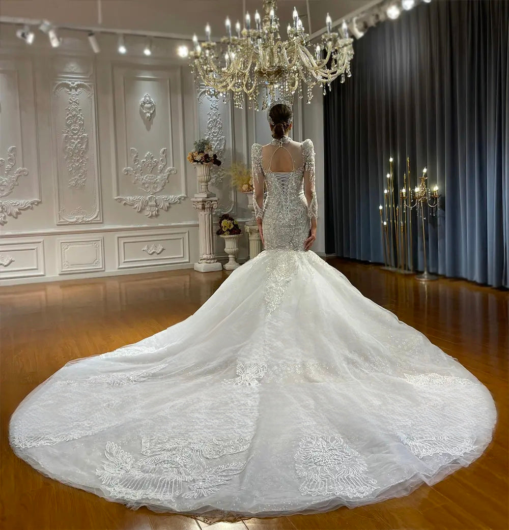 Rear view of a luxury mermaid bridal gown highlighting a keyhole open-back design, a lace-up corset closure, and a wide circular train with delicate floral lace appliqués.