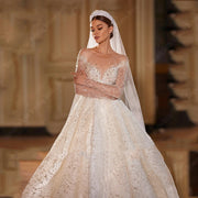 A bride wearing a luxury V-neck wedding dress with bright sequins, long sleeves, and a grand A-line silhouette, paired with a matching veil and headpiece.