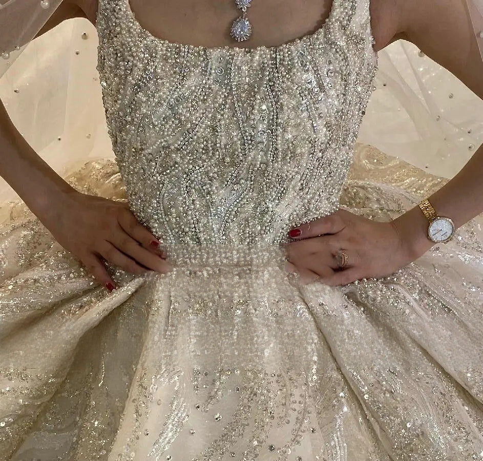 Detailed close-up of a bride wearing a sleeveless beaded wedding dress bodice, highlighting the dense, handcrafted pearl and crystal embellishments and the classic square neckline.