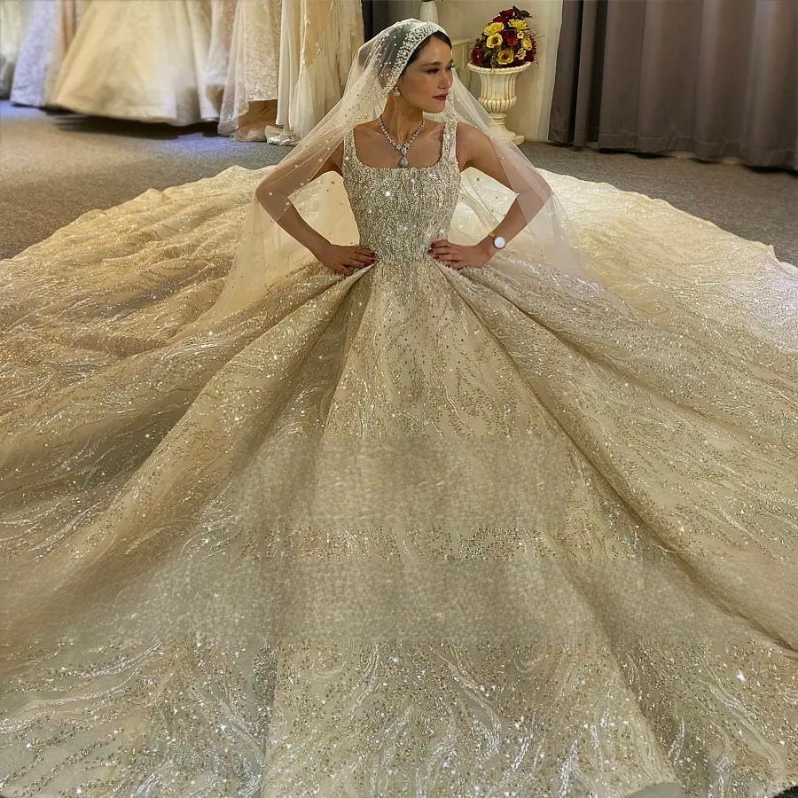 Breathtaking high-angle shot of a bride sitting in a luxury champagne ball gown wedding dress, displaying the massive circular spread of the sparkling, fully beaded skirt and veil on the floor.