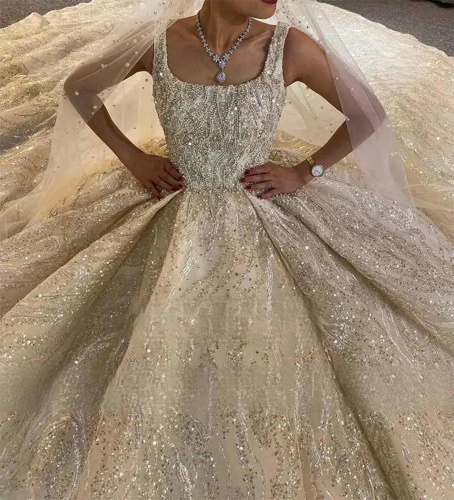 Close-up front view of an elegant bride's upper torso, wearing a heavily beaded luxury vintage sleeveless wedding dress, paired with a matching pearl-drop necklace and sheer bridal veil.