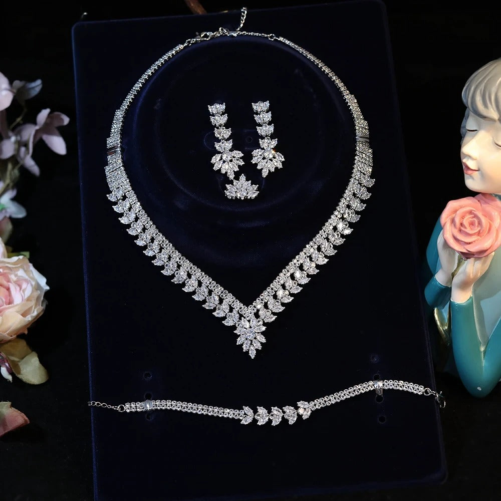 Direct front view of a premium cubic zirconia bridal jewelry collection featuring a marquise cluster necklace, matching bracelet, and water drop earrings on a dark blue velvet display plaque.