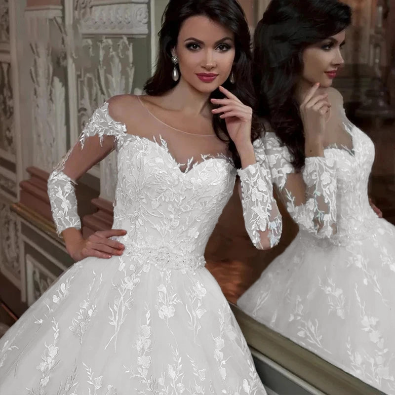 A front view of a bride wearing a luxury ball gown wedding dress with detailed embroidery, sheer full sleeves, and an elegant O-neck design.