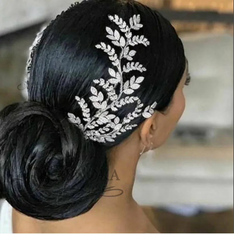 Rear side portrait of a bride showing a luxury wedding hair accessory pin with an elongated silver leaf branch design tucked into a classic low bun.