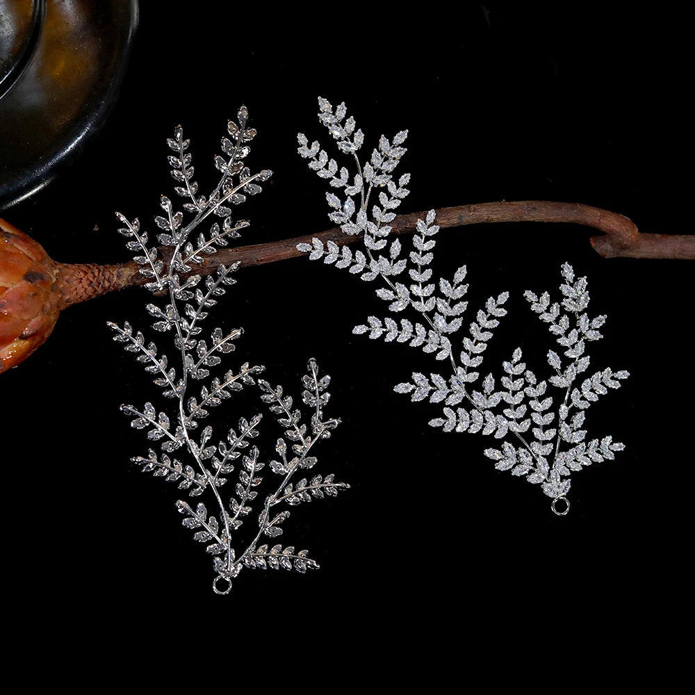 Top-down flat lay view of two matching silver-plated crystal bridal hairpins with intricate botanical vine structures on a black background.