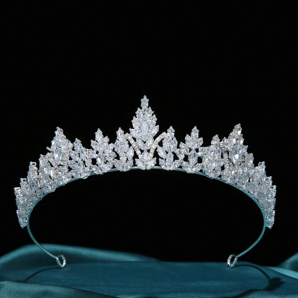 A stunning silver-tone luxury zircon tiara crown for women resting on an emerald green satin sheet.