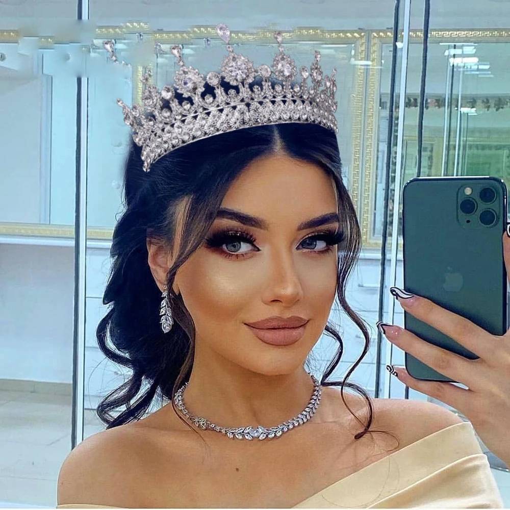 A woman taking a selfie while wearing a high luxury zircon crystal bridal tiara headband with a matching crystal necklace and earrings.