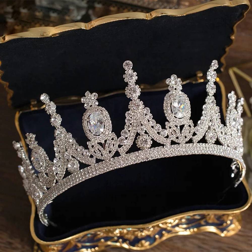 A premium silver zircon bridal tiara crown displaying alternating oval-cut gemstones, nestled inside a luxury blue and gold velvet jewelry box.
