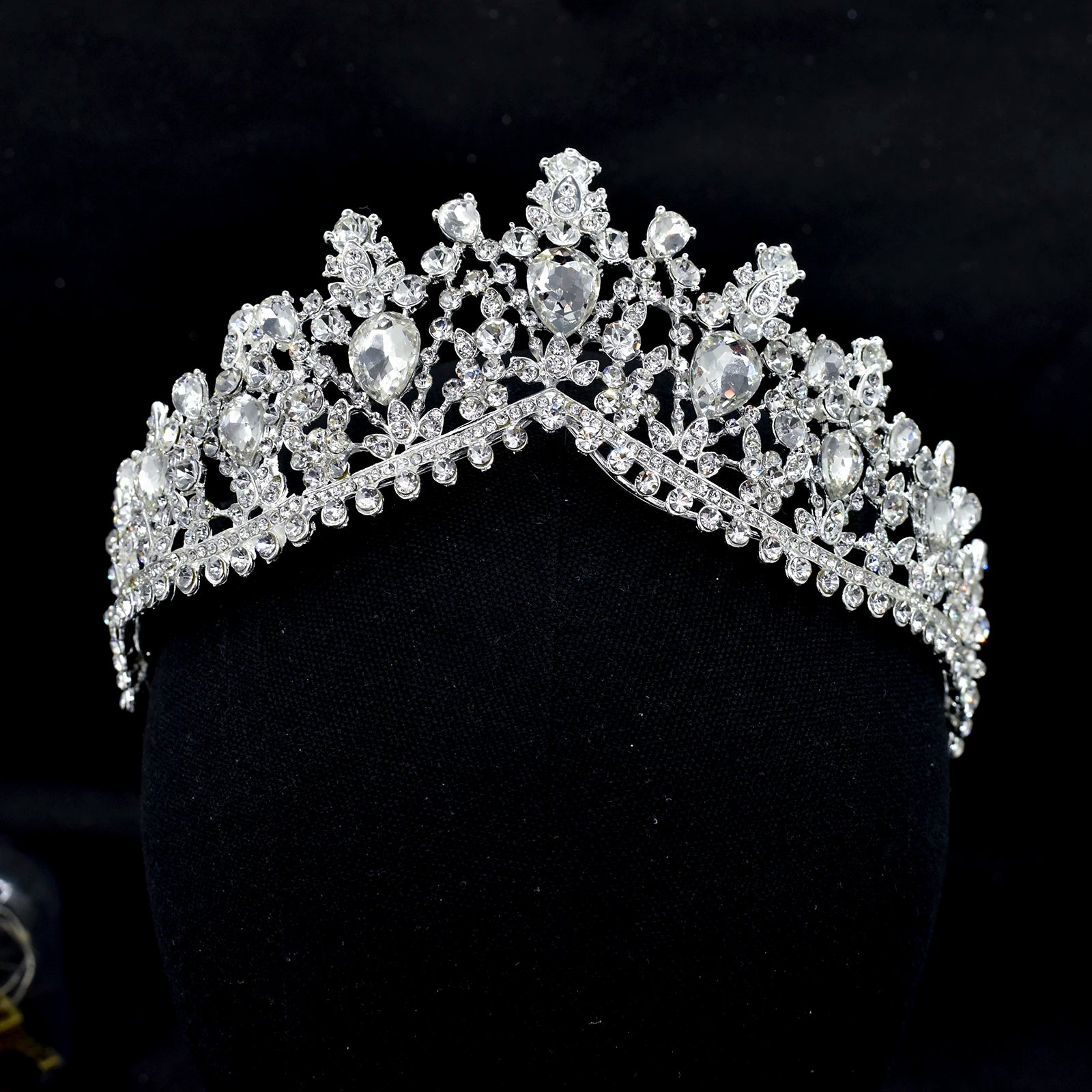 Front close-up view of a sparkling silver zircon bridal tiara crown with teardrop crystal accents on a black mannequin display stand.