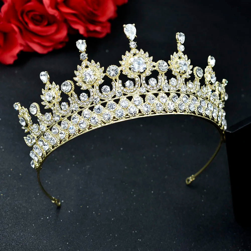 A luxury gold-plated zircon bridal tiara crown with intricate floral and scrollwork detailing showcased on a dark reflective surface.