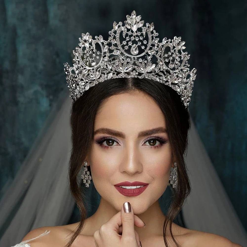 Front-facing portrait of a bride wearing an ornate silver zircon crystal bridal tiara crown, complete with matching dropdown earrings and a veil.