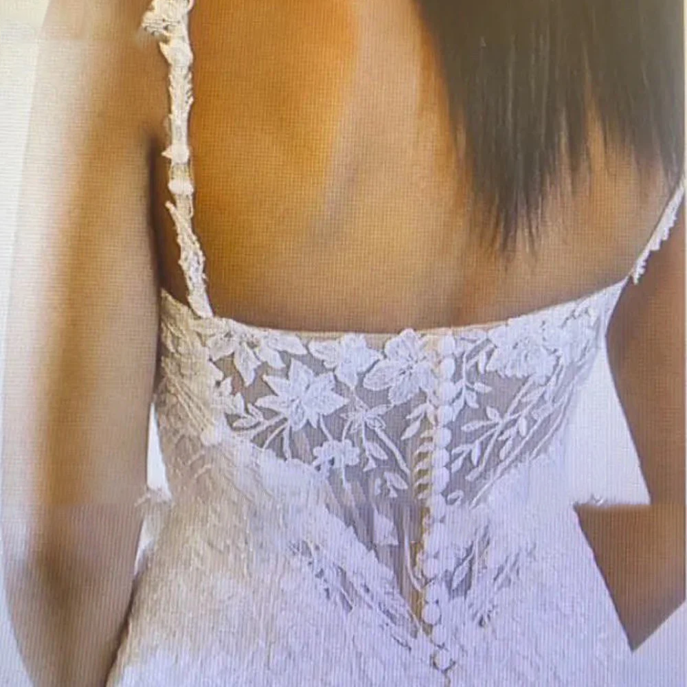 A detailed look at the back of a beaded, lace applique wedding gown featuring a delicate strap design and intricate embroidery.
