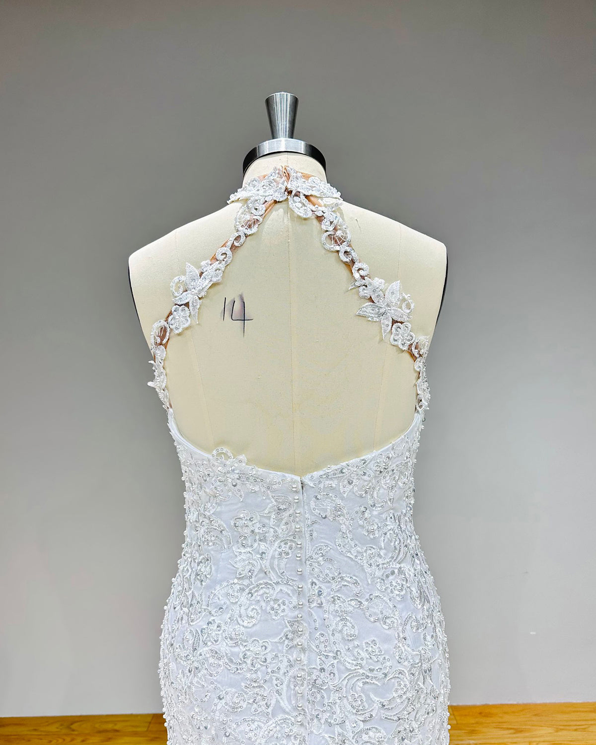 Close-up of the backless design on a halter wedding dress bodice highlighting the delicate lace strap borders and fabric-covered bridal buttons over a zipper closure.