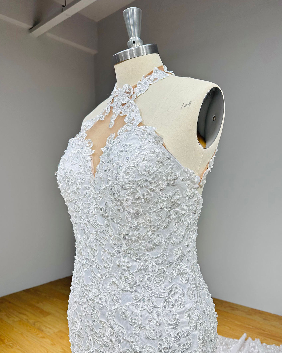 Side angle close-up of a bridal gown bodice emphasizing the dense floral lace appliques, intricate pearl beadwork, and sheer illusion halter neckline.