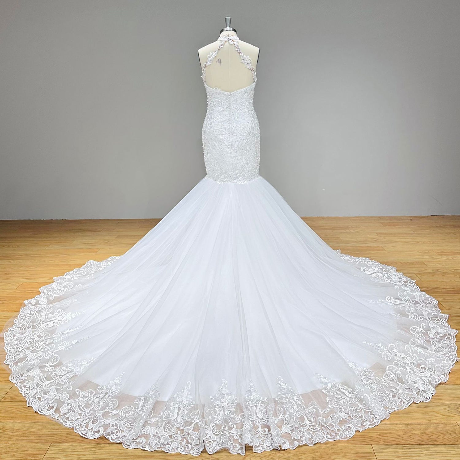 Full back view of a lace halter mermaid bridal gown showcasing a low open backless cutout and a wide tulle train detailed with an embroidered lace border.