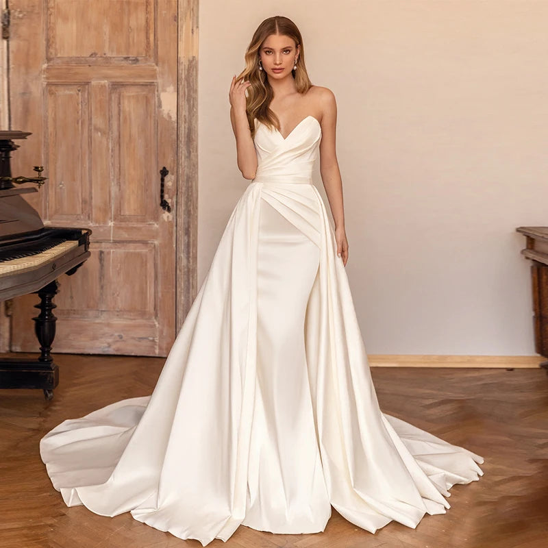 A bride wearing an elegant satin mermaid wedding dress with a detachable train, featuring a chic sweetheart neckline and a sophisticated silhouette.