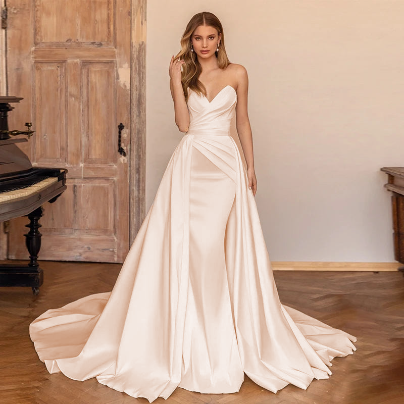 A portrait of a bride posing by a piano in a sweetheart satin mermaid wedding dress, showcasing the gown's flattering drape and fit.