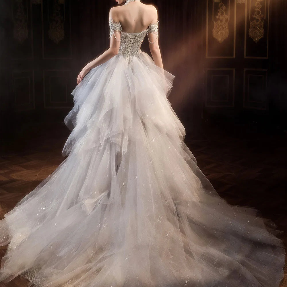 Back view of an elegant mermaid bridal gown featuring a lace-up corset back, off-the-shoulder straps, and a dramatic, voluminous tiered tulle detachable overskirt.